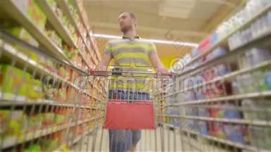 一个人带着满满的超市手推车，走近摄像机，开心地笑着，年轻人在超市里挑选产品